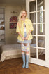 Woman in a yellow shirt and denim skirt standing in a room with wooden floor and large mirror.